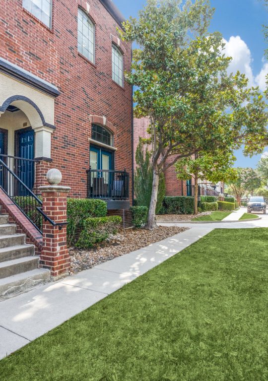 the front yard of a brick apartment building with grass and a green lawn at The  Ellington